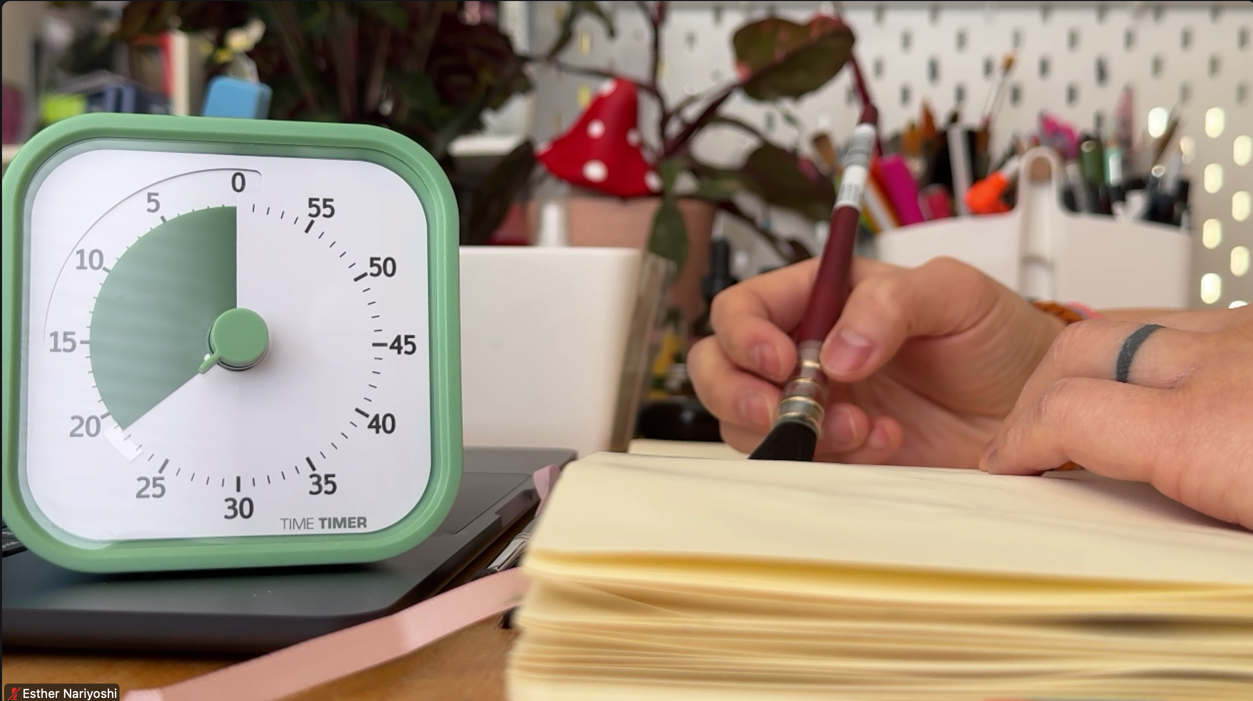 Timer on a desk with a hand holding a pen and a notebook