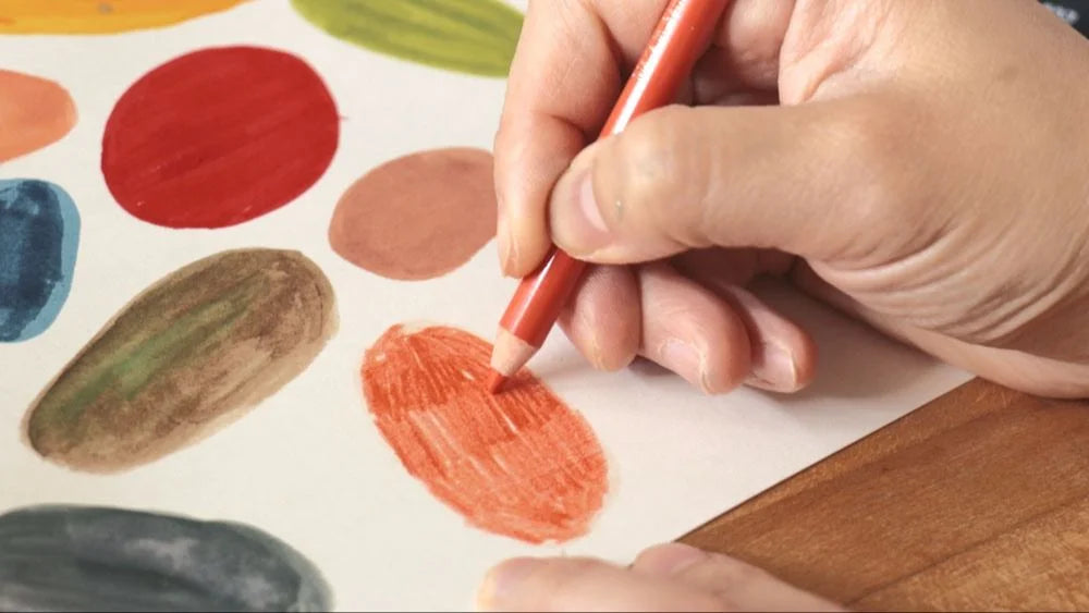 Hand holding a red marker over a piece of paper with colorful paint swatches.