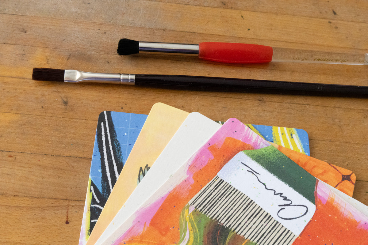 Illustrated postcards fanned out next to paintbrushes