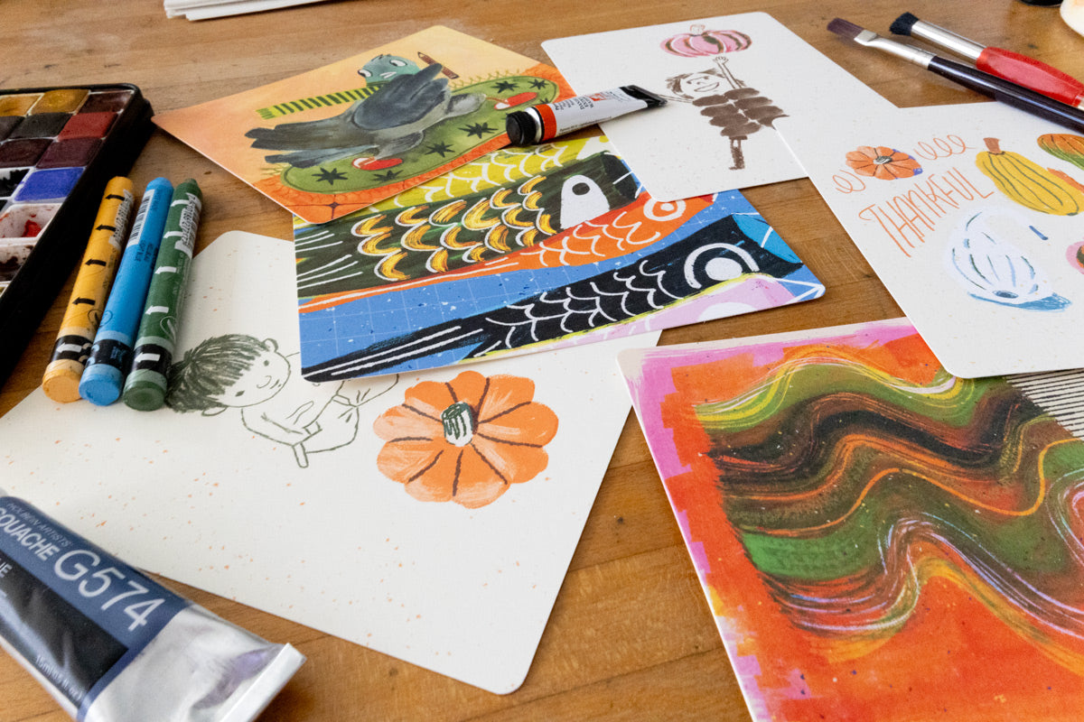Monthly Postcard Club cards arranged with pencils, crayons, and art supplies